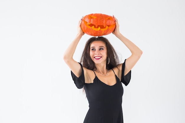 Foto mulher gótica bonita com roupas de estilo halloween com abóbora nas mãos, luz de fundo com espaço de cópia