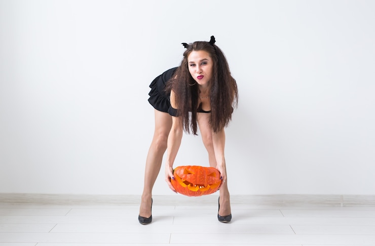 Foto mulher gótica bonita com roupas de estilo halloween com abóbora nas mãos, luz de fundo com espaço de cópia