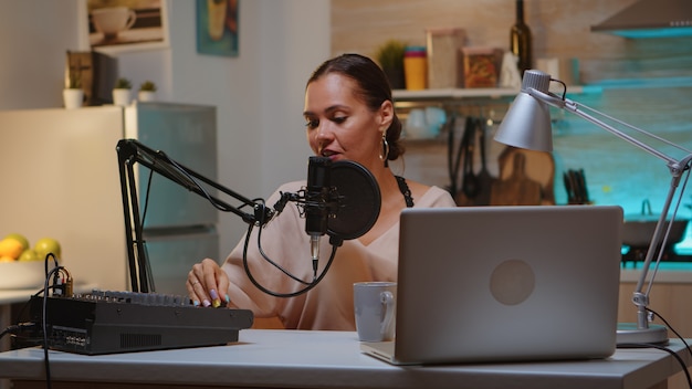 Mulher gravando som em home studio para podcast. Apresentador de show online criativo, vídeo, estação de produção de som em casa, noite de estilo de vida, web, internet, equipamento de mídia, laptop.