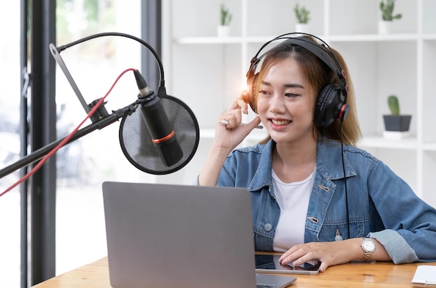 Mulher gravando um podcast em seu laptop com fones de ouvido e um microscópio podcaster feminina fazendo podcast de áudio de seu estúdio em casa