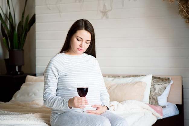 Foto mulher grávida a beber um copo de vinho vermelho.