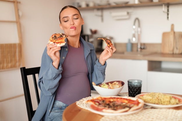 Mulher grávida apreciando duas fatias de pizza na cozinha