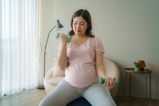 Mulher grávida asiática fazendo exercício com halteres na sala de estar em casa conceito saudável