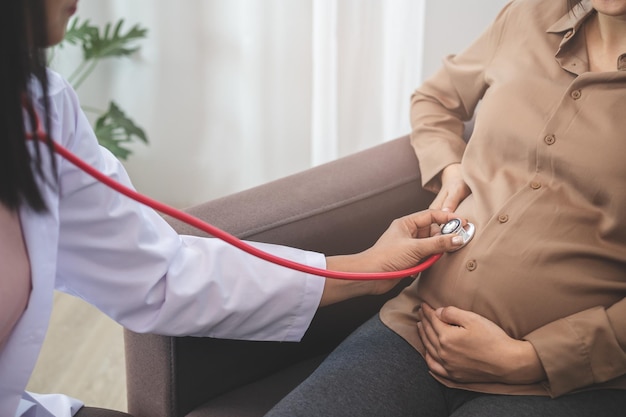 Mulher grávida asiática sendo examinada pelo médico, usando estetoscópio para verificar a barriga e deseja verificar o crescimento do feto.