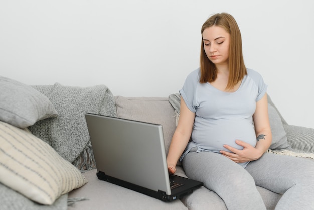 Mulher grávida atraente tocando a barriga e usando o laptop na cama