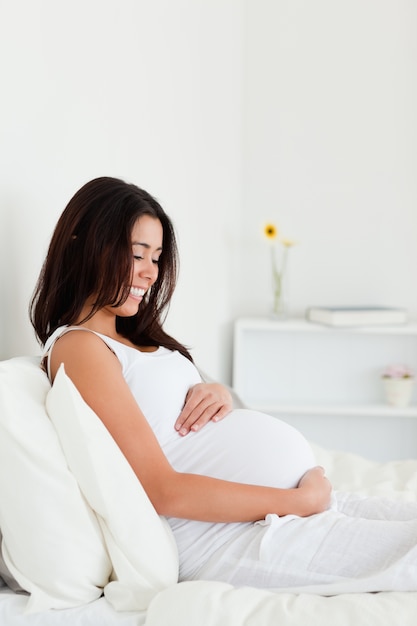 Mulher grávida atrativa tocando sua barriga enquanto deita em uma cama