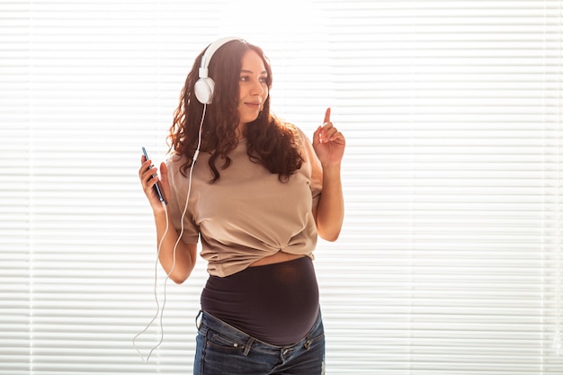 Mulher grávida bonita e pacífica ouve música clássica agradável usando smartphone e