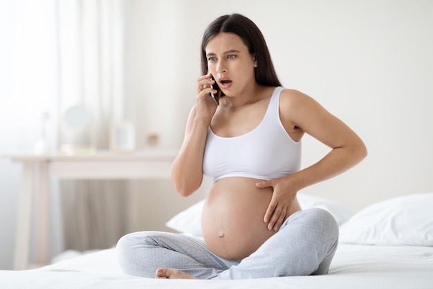 Mulher grávida chocada sentindo alguma dor e desconforto ligando para o médico