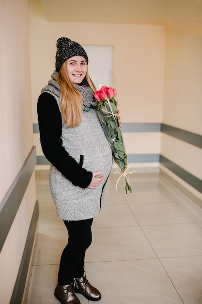 Mulher grávida com casaco de inverno e gorro quente no hospital. menina com flores. dia de nascimento. aniversário.