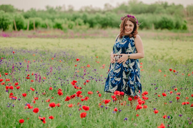 Mulher grávida com flores silvestres na cabeça em um prado cheio de papoulas e segurando uma foto de ultrassom de seu bebê