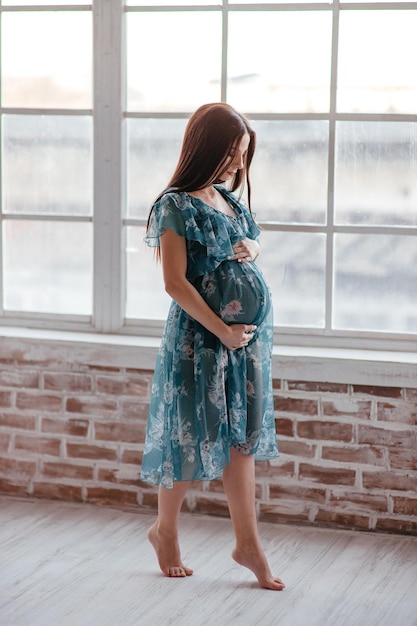 Mulher grávida com longos cabelos loiros em um vestido turquesa olha de barriga para baixo e gruda nele