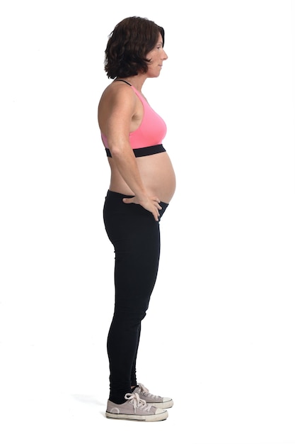 Mulher grávida com roupa esportiva isolada no fundo branco, vista lateral e mãos no quadril