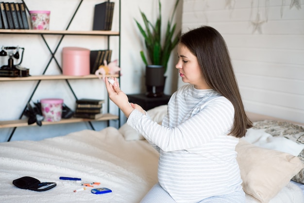 Mulher grávida com seringa de insulina em casa na cama. conceito de diabetes grávida.