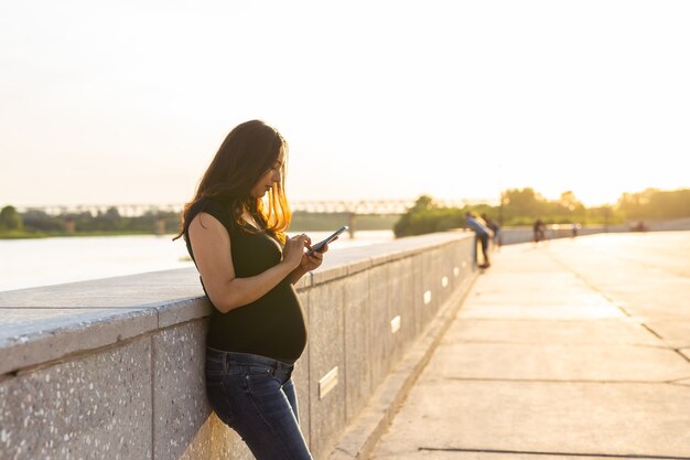 Mulher grávida com smartphone ao ar livre, tecnologia de gravidez e conceito de comunicação