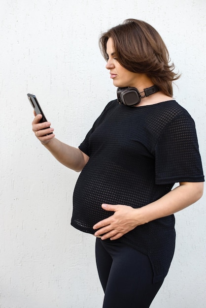 Foto mulher grávida com smartphone e fones de ouvido ao ar livre em fundo branco saúde mental da maternidade e conceito de gravidez mídias sociais internet negócios conversando em telefone móvel