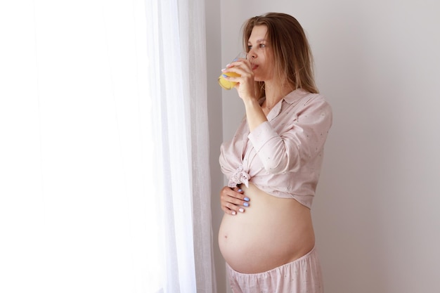 Mulher grávida com suco de laranja pela janela