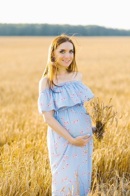 Mulher grávida concurso andar em um campo. Senhora de vestido azul. Hora de relaxar. Mulher está esperando por um bebê