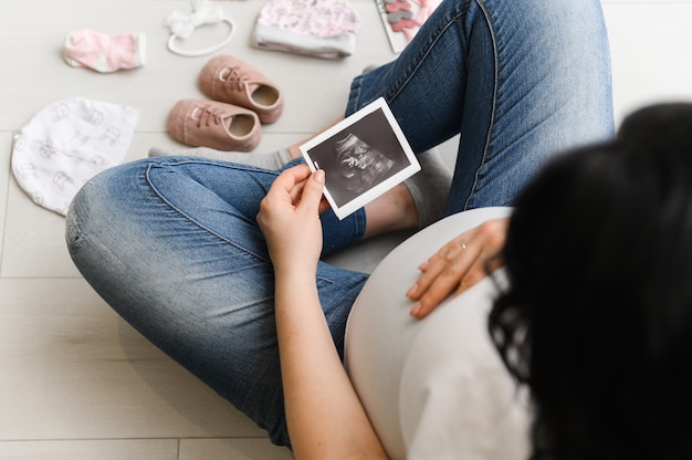 Foto mulher grávida curtindo a futura maternidade com a primeira foto de ultrassom de seu bebê, vista superior