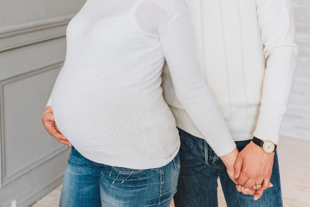 Mulher grávida de mãos dadas com o marido, vestindo jeans e blusas brancas.