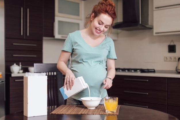 Mulher gravida de sorriso que prepara o café da manhã