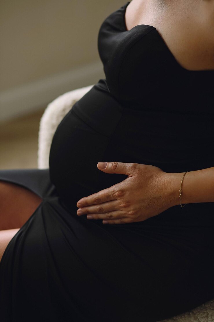 Foto mulher grávida de vestido preto sentada na cadeira em casa e segurando sua barriga grávida