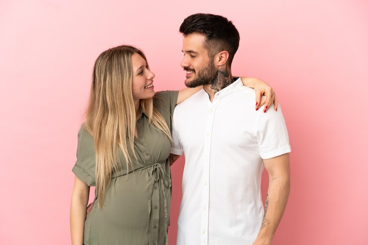 Foto mulher grávida e homem sobre fundo rosa isolado felizes e rindo