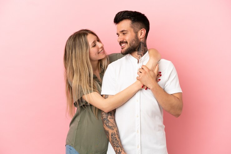 Foto mulher grávida e homem sobre fundo rosa isolado rindo e se abraçando