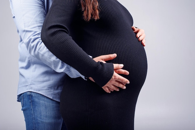 Mulher grávida e seu marido de mãos dadas em sua barriga conceito de gravidez feliz