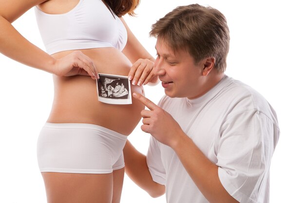 Mulher grávida e seu marido estão segurando sua barriga e uma foto de seu ultrassom
