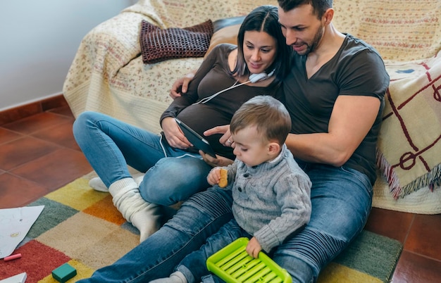 Mulher grávida e seu marido olhando para o tablet enquanto seu filho brinca