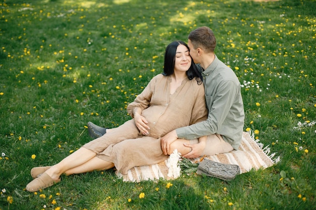 Mulher grávida e seu marido sentado em um parque em uma grama e abraçando