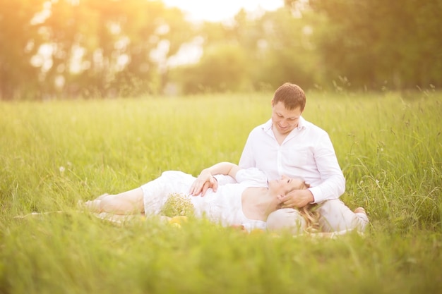 mulher grávida e seu marido sentam-se na grama do parque.