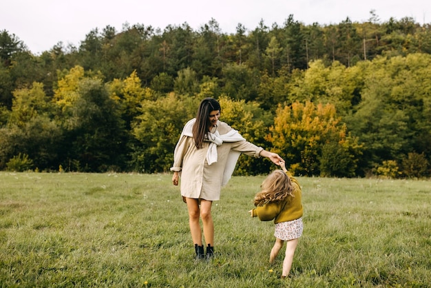 Mulher grávida e sua filha dançando ao ar livre em um campo com grama verde