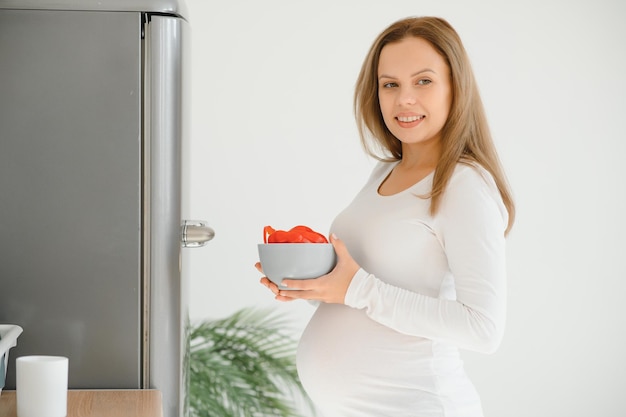 Mulher grávida em casa na cozinha abre a geladeira