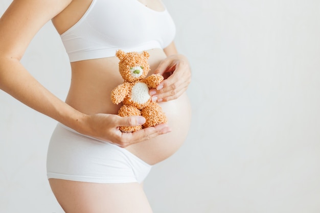 Mulher grávida em cueca branca com urso de brinquedo