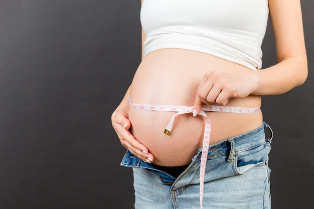 mulher grávida em jeans abertos, medindo sua barriga