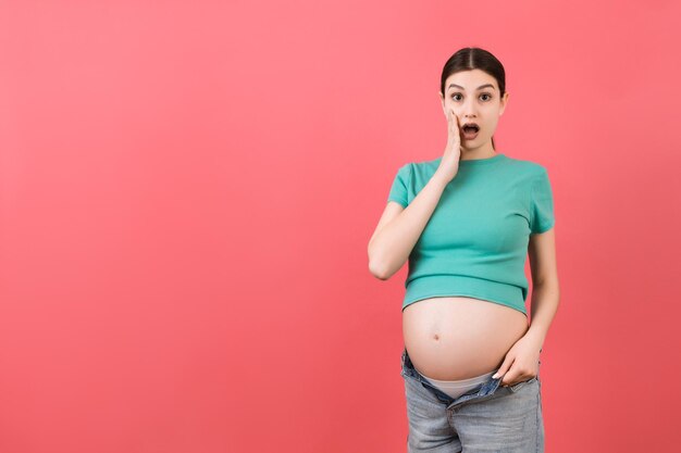 Foto mulher grávida em jeans sem zíper mostrando sua barriga nua em fundo colorido com espaço de cópia conceito de espera de bebê