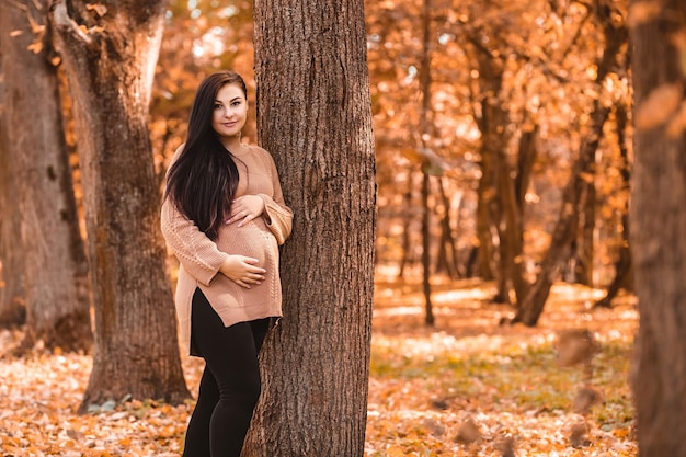 Mulher grávida em pé na floresta do parque da cidade do outono, segurando acariciando sua barriga redonda