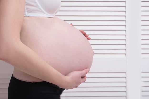 Mulher grávida em roupa interior, abraçando a barriga com as mãos