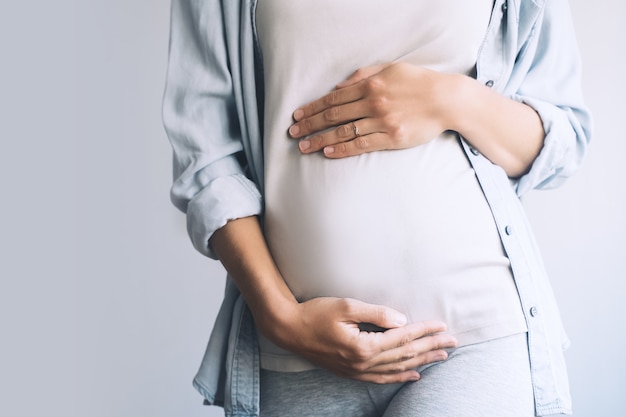 Mulher grávida em roupas casuais de mãos dadas na barriga no fundo branco