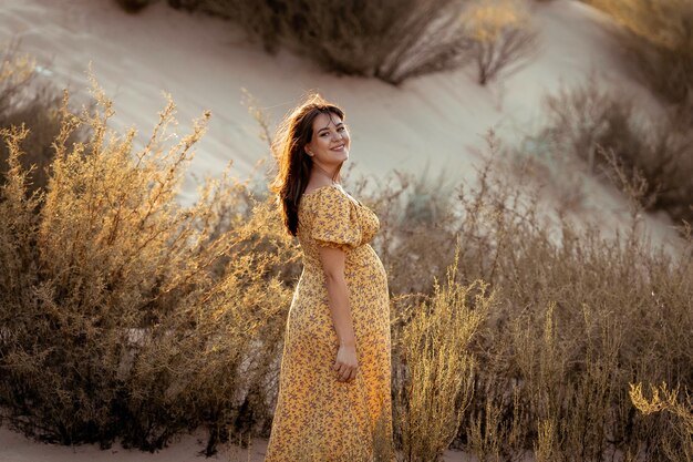 mulher grávida em um vestido amarelo na praia é alegre