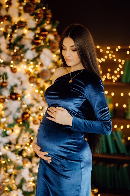 Foto mulher grávida em um vestido azul com luzes de natal atrás dela