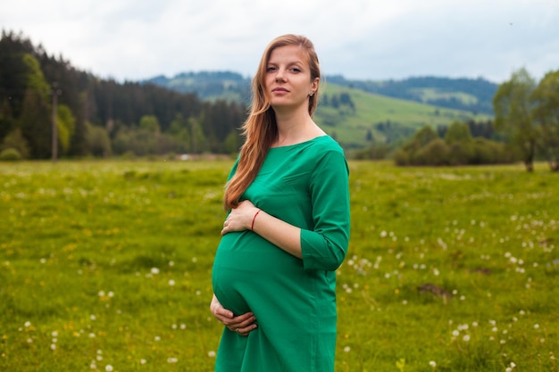 Mulher grávida em uma túnica verde está respirando ar limpo no fundo da natureza