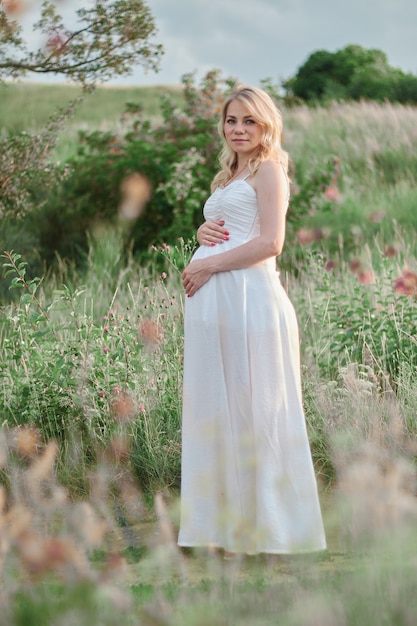 Mulher grávida em vestido branco posando no parque