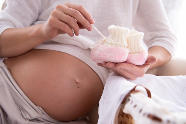 Mulher grávida está segurando sapatos para o futuro bebê