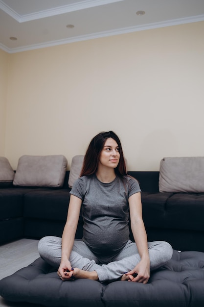 Mulher grávida esticando braços e pernas fazendo treino pré-natal em casa no tapete de ioga foco seletivo