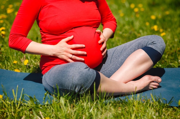 Mulher grávida fazendo asana sukhasana ao ar livre