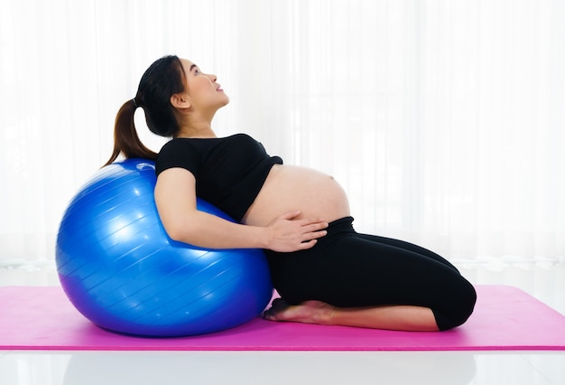 Mulher grávida fazendo exercícios de ioga em uma bola de fitness na sala de estar em casa