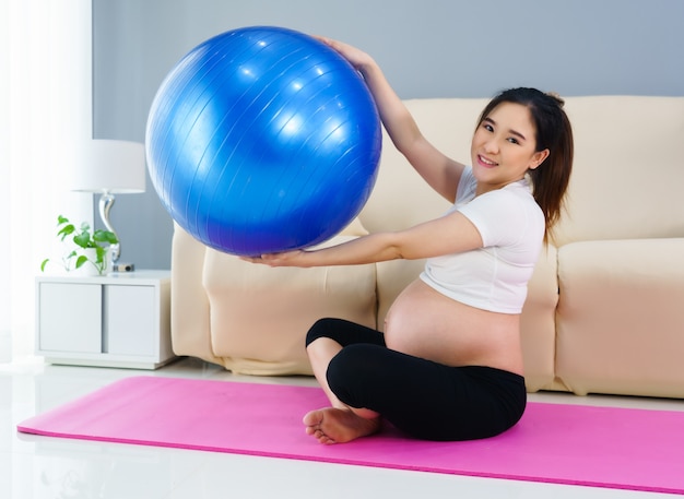 Mulher grávida fazendo exercícios de ioga em uma bola de fitness na sala de estar em casa