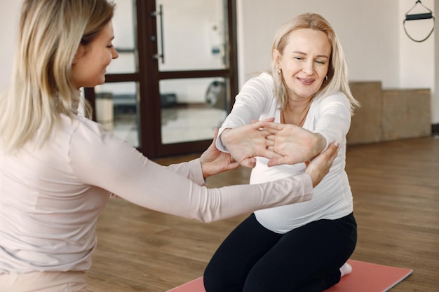 Mulher grávida fazendo ioga com personal trainer Instrutor de ioga auxiliando a mulher grávida enquanto fazia exercícios Mulher grávida loira vestindo roupas brancas